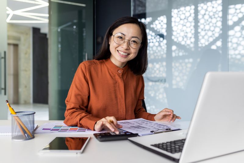 Portrait of young Asian successful accountant working on paperwork with calculator inside office